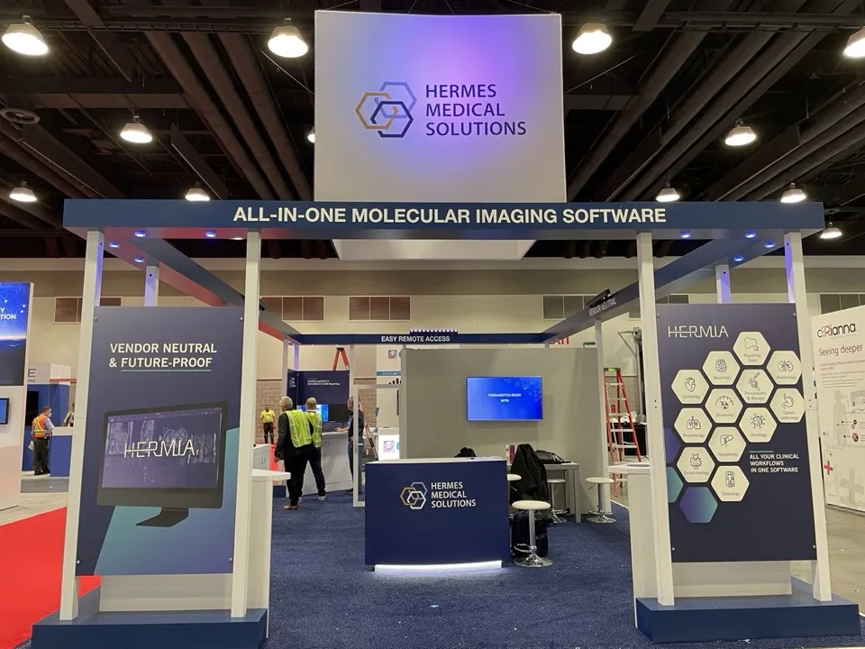 The Hermes Medical Solutions exhibit open on a show floor, with staff and visitors at the screens.