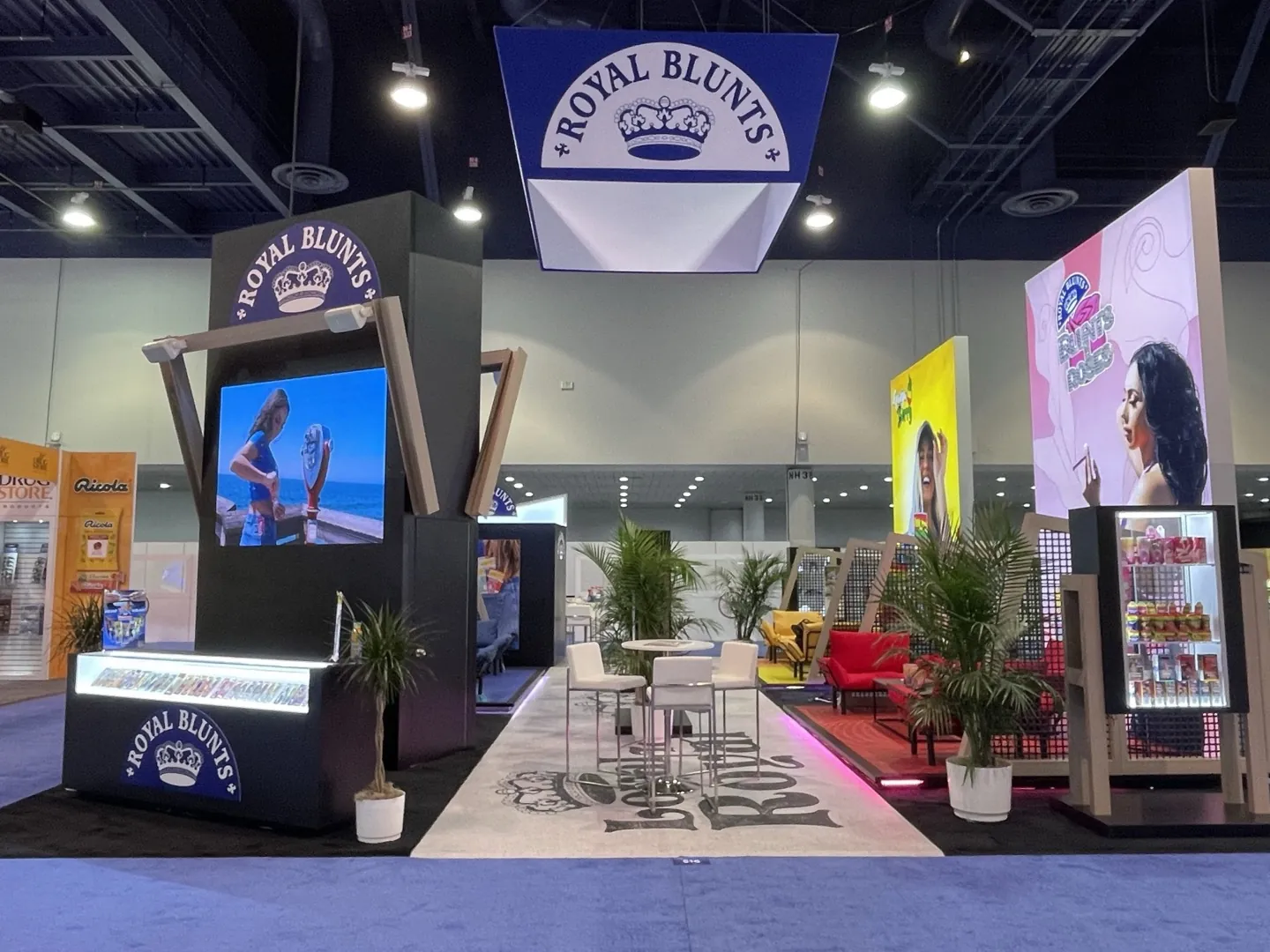 A large illuminated island exhibit for Royal Blunts on a trade show floor, with lit brand towers, video screens and a seating lounge.