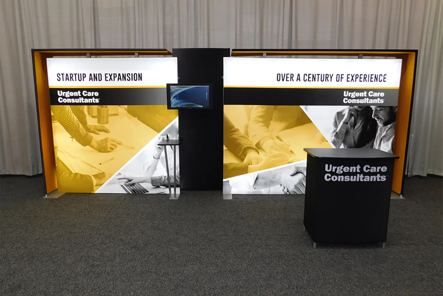 The Urgent Care Consultants exhibit: two backlit graphic walls and a counter, on a show floor.